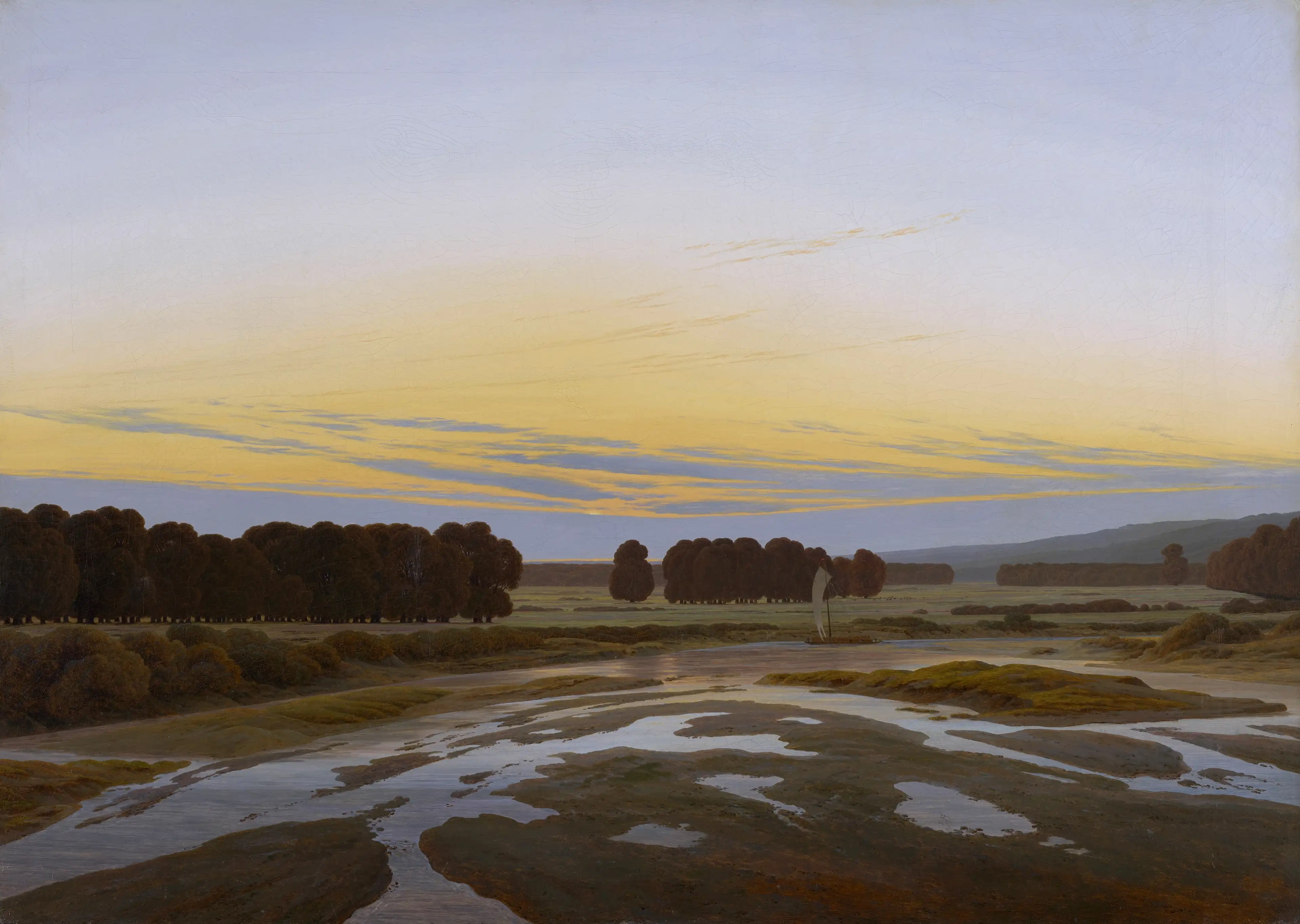 Die Abbildung zeigt das Ölgemälde »Das Große Gehege bei Dresden« von Caspar David Friedrich. Zu sehen ist eine friedliche Landschaftsszene in einem breiten Querformat. Im Vordergrund öffnet sich eine zerklüftete Flusslandschaft, durchzogen von erdigem Boden, Grasland und den Himmel spiegelnden Wasserflächen. Im Hintergrund öffnet sich ein weites Landschaftspanorama mit Baumreihen und einem großzügigen Himmel, in dem gelbe und blaue Farbtöne sanft ineinander übergehen, begleitet von zarten Lilatönen. Aus einer leicht erhöhten Perspektive eingefangen, zeigt das Gemälde eine Welt im Übergangszustand.