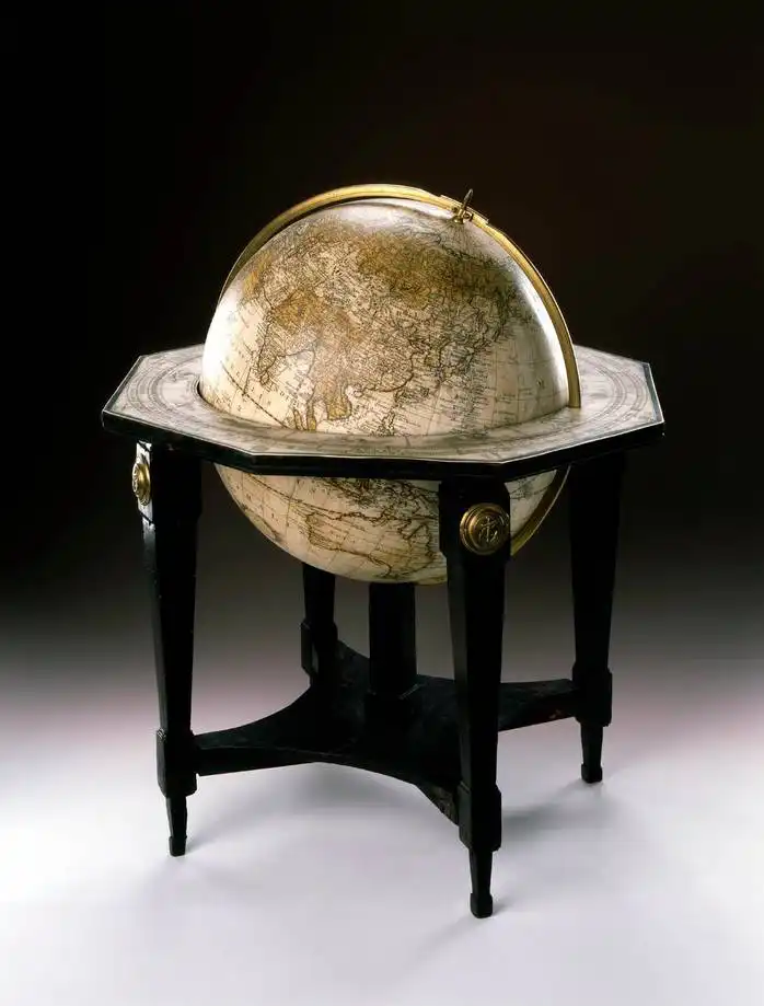 Zu sehen ist ein Foto eines historischen Globus, ein Modell der Erdkugel von 1792. Die Oberfläche der 32 cm durchmessenden Kugel ist aus einzelnen Karten auf Papier zusammengesetzt. Der Globus wird von einem Gestell aus schwarzem Holz und Messing gehalten.